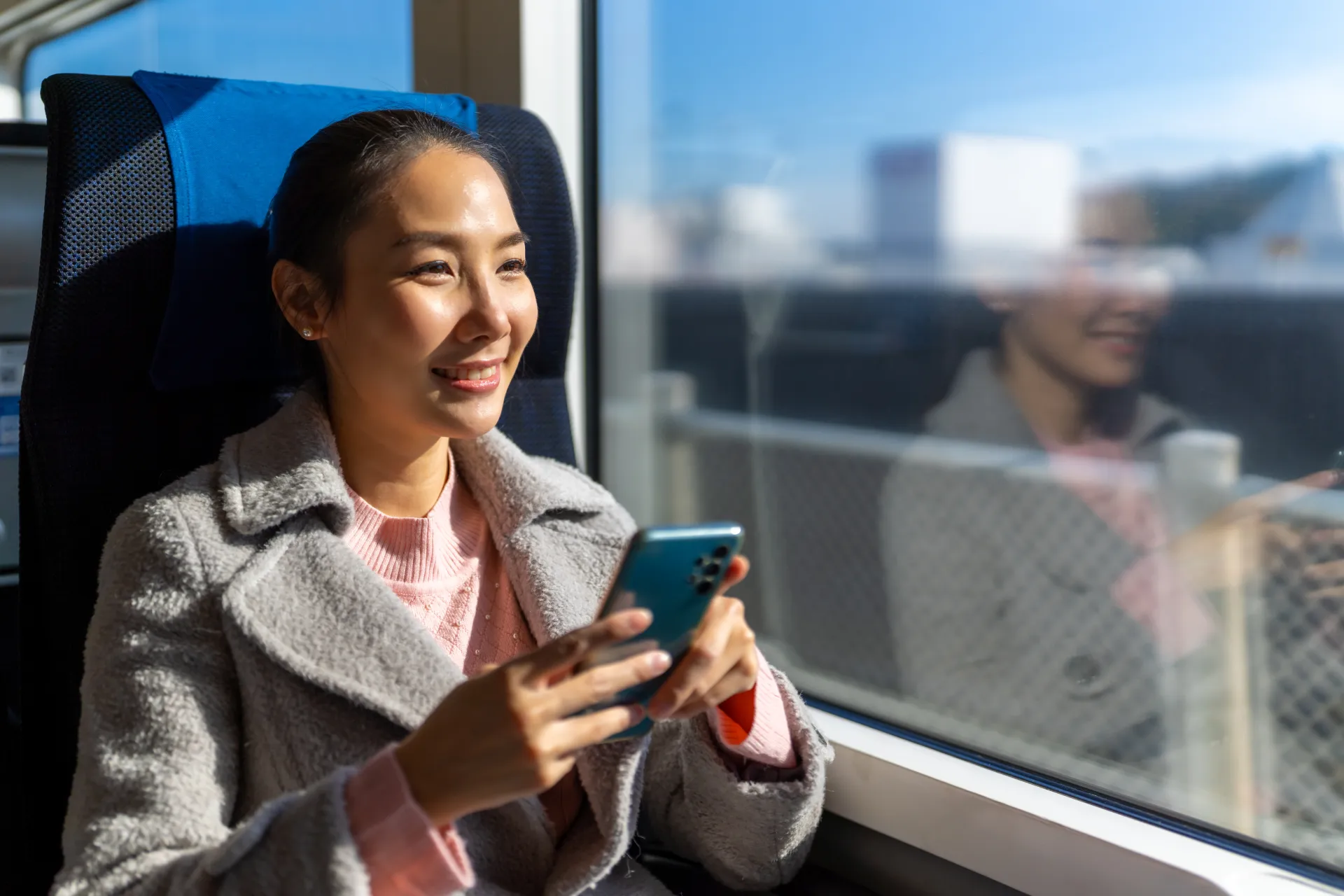 A confident-looking student is sitting in a train. They are smiling while using their smartphone.